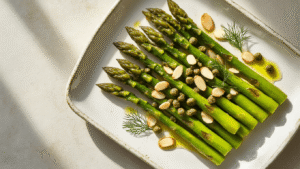 Geroosterde Groene Asperges met Amandelen: Een Verrukkelijk en Snel Bijgerecht Cinematic overhead shot of roasted green asparagus garnished with almonds and capers on a rustic ceramic platter, with natural light highlighting the dish's textures and a soft, moody atmosphere.