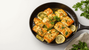 Gebakken Kabeljauw met Kruiden - Mals, Sappig en Klaar in 30 Minuten Cinematische close-up van gebakken kabeljauwfilets in een gietijzeren pan, omringd door verse kruiden en citroen, met warme amber verlichting en stoom die subtiel opstijgt.