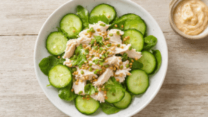 Komkommer Tonijnsalade: De Ultieme Verfrissende Lunch Verfrissende komkommer-tonijnsalade met mayonaise en mosterd in een witte kom, op een rustieke houten tafel met zachte natuurlijke verlichting.